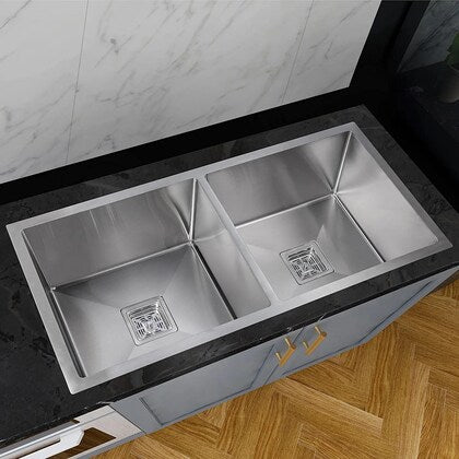 Stainless steel kitchen sink with a marble countertop and wooden floor.